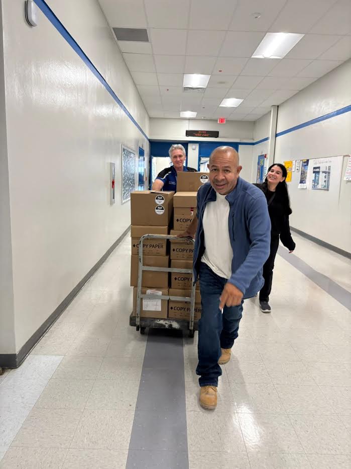Volunteers wheeling a hand truck stacked with boxes down a Westglades Middle School hallway