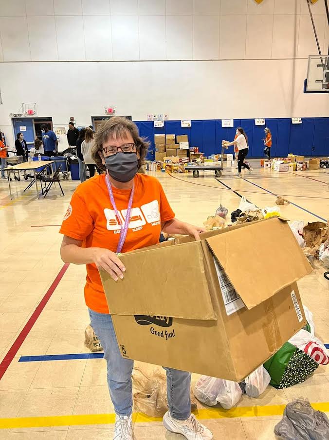 Westglades Middle School volunteer in a face mask unpacking a large cardboard box in the gym