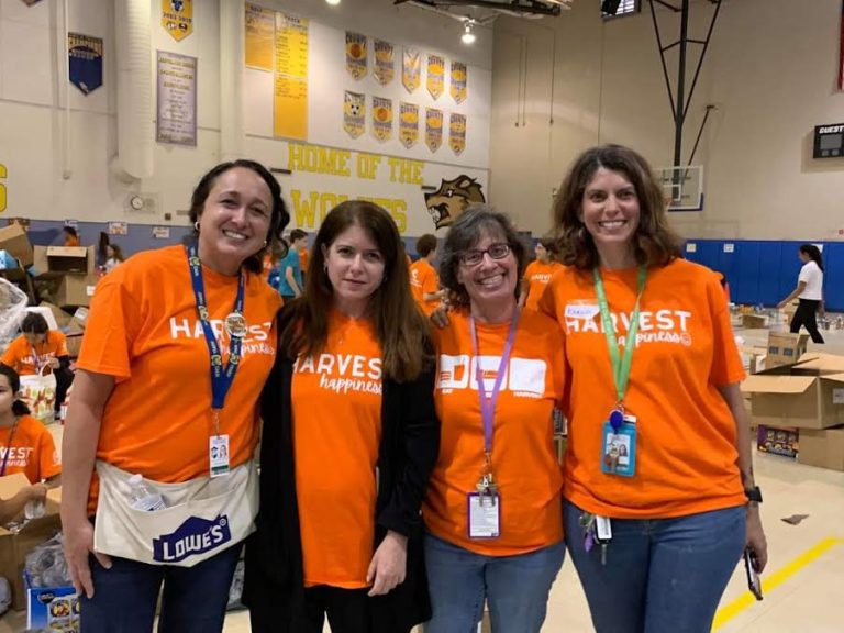 Four Westglades Middle School volunteers in orange Harvest shirts and Lowe's aprons in the gym