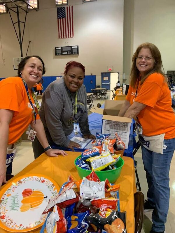 Westglades Middle School volunteers arranging snacks on a table with an orange tablecloth