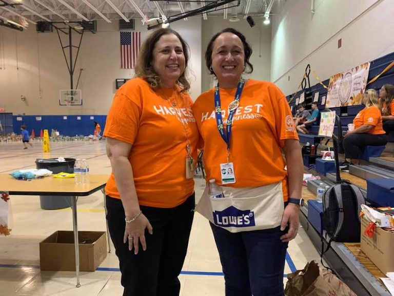 Two Westglades Middle School volunteers in orange shirts and lanyards smiling in the gym