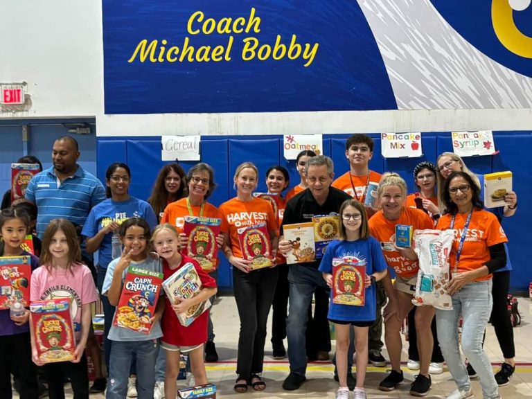 Children and volunteers holding up cereal boxes in the Westglades Middle School gym